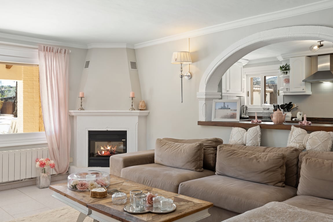Bright living area featuring a corner fireplace, neutral-toned modular sofa, and a classic white archway opening into the kitchen.