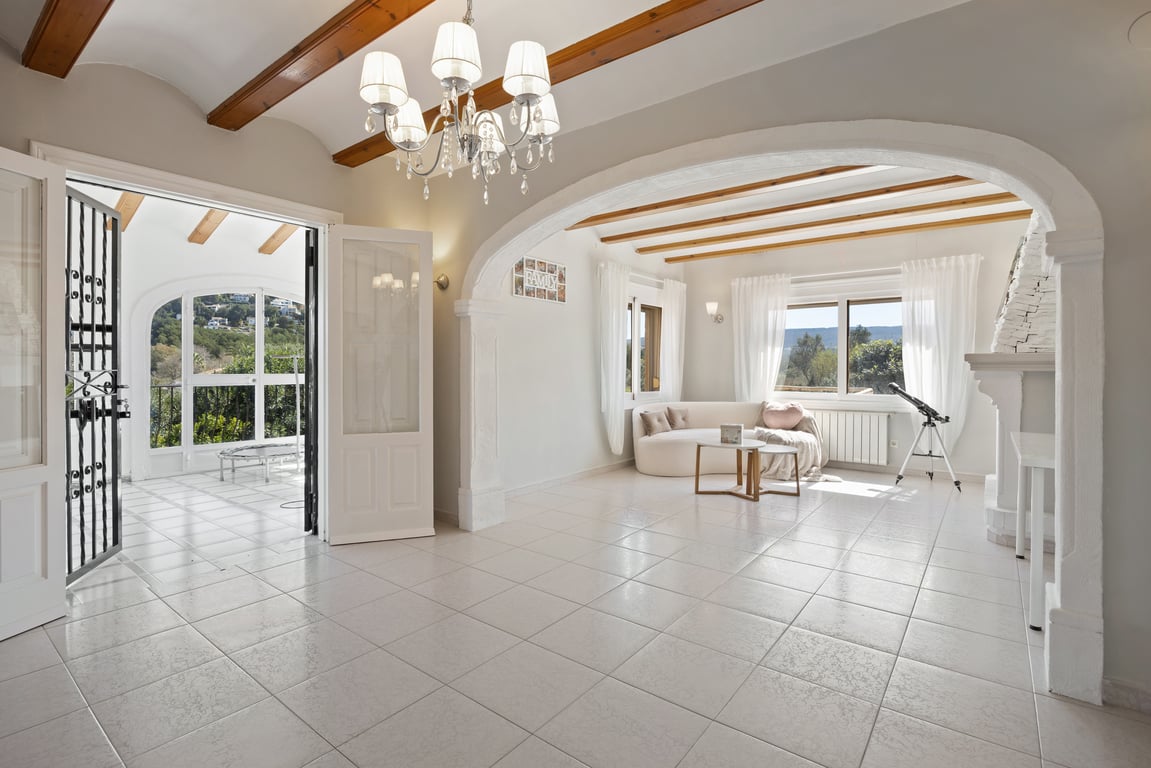 Bright living area featuring exposed wooden beams, a white stone fireplace, and a large archway leading to a seating nook with views of the countryside.