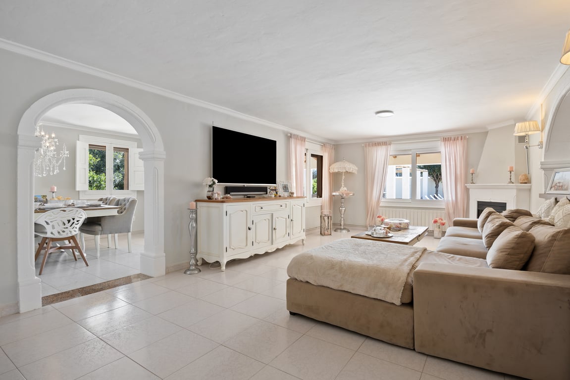 Bright living room featuring ceramic floors, a corner sofa, and a fireplace. A decorative archway leads to the dining area, emphasizing the open-plan layout and natural light.