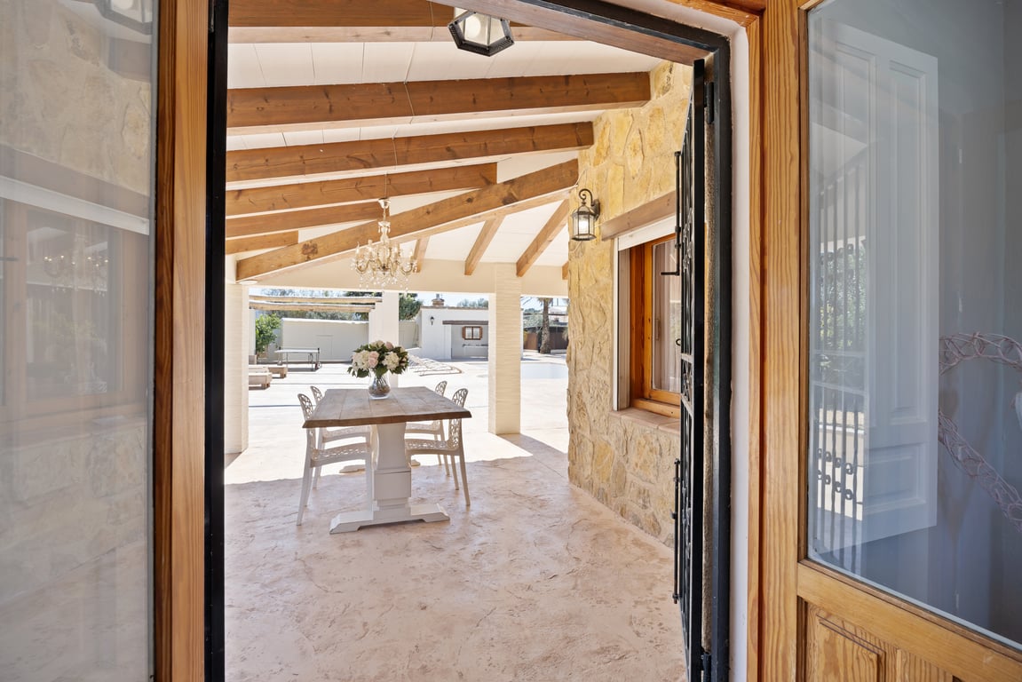 Covered terrace featuring exposed wooden beams, natural stone walls, and an outdoor dining area overlooking the pool zone.