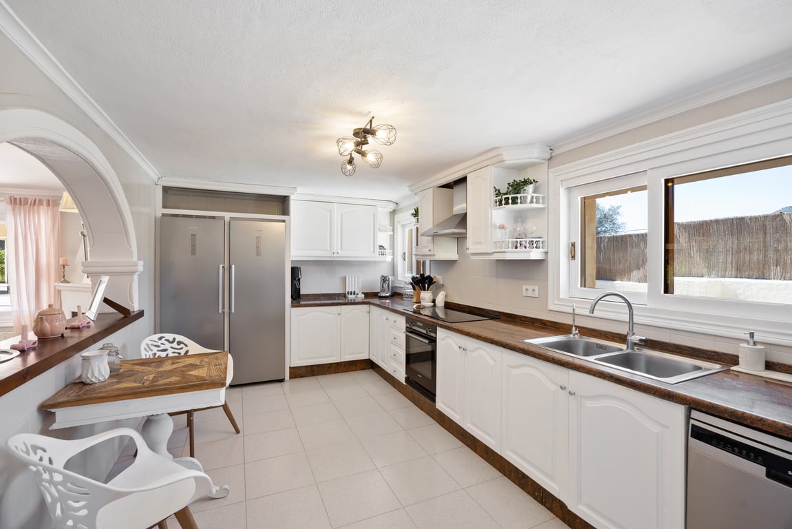 Fully equipped kitchen with white cabinetry, dark wood countertops, and stainless steel appliances, featuring a breakfast nook and a traditional archway.