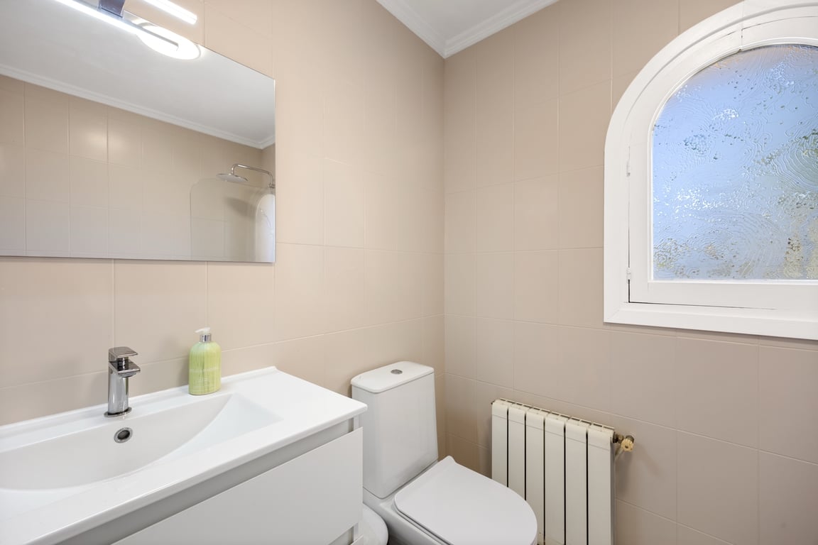 Functional bathroom featuring neutral tiling, a white vanity unit, radiator, and a characteristic arched window with frosted glass for privacy and light.