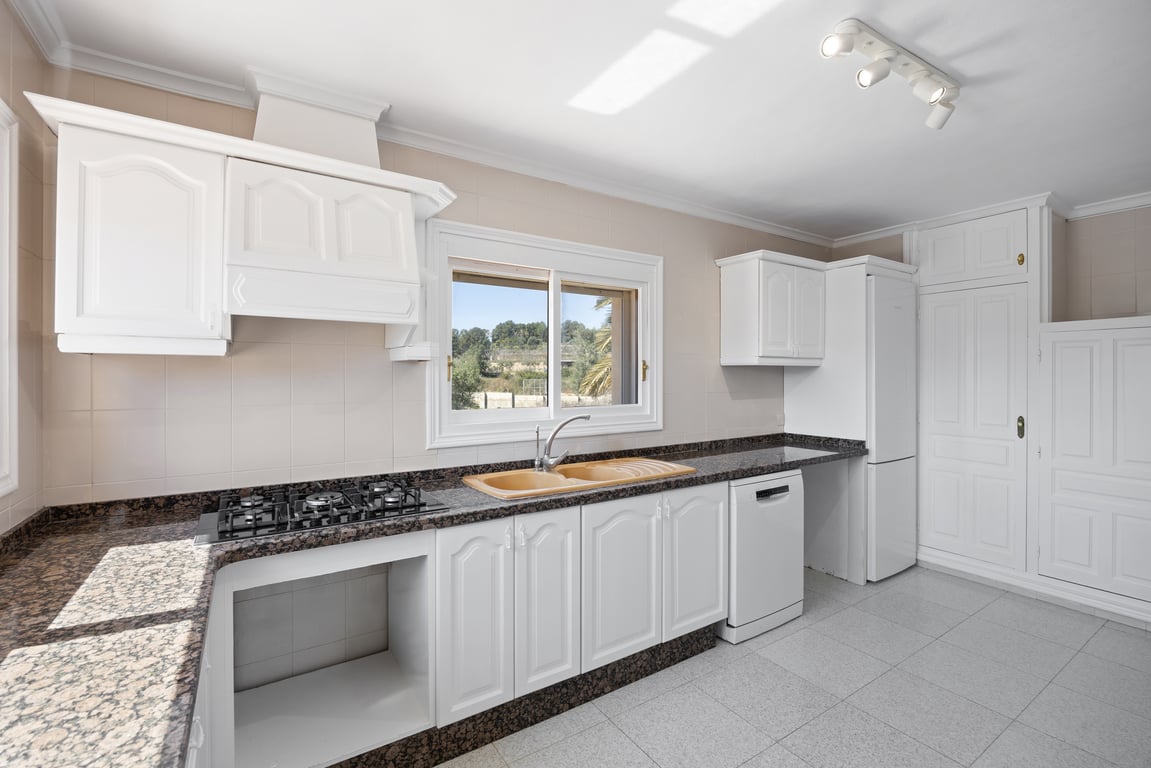 Functional kitchen featuring white cabinetry, dark granite countertops, and a double sink. Includes a gas cooktop, classic extractor hood, and a window with garden views.
