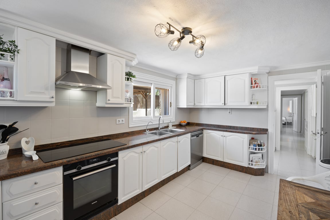 Functional kitchen with traditional white cabinetry, dark granite countertops, and stainless steel appliances. Features include a window over the sink and a modern industrial ceiling light.