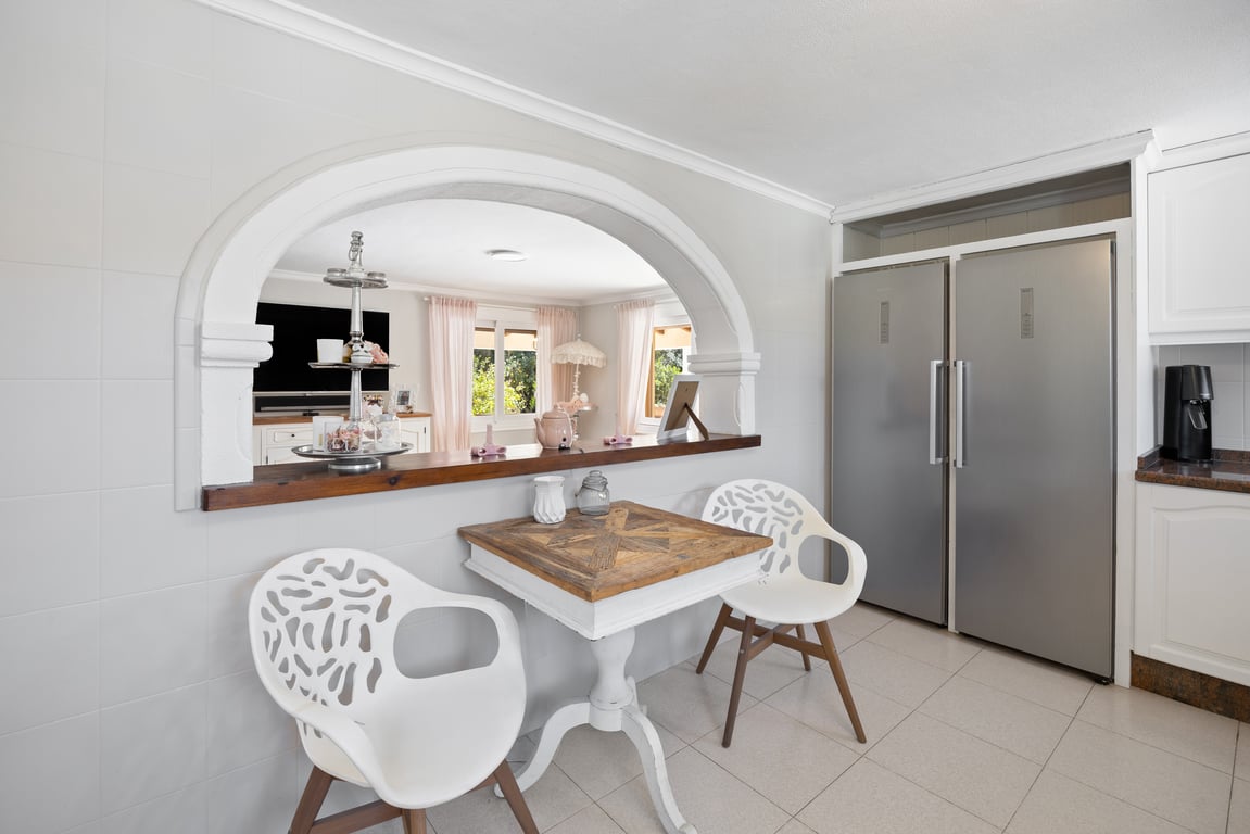 Kitchen featuring an arched pass-through to the living area, a double stainless steel refrigerator, and a breakfast nook with a rustic wooden table.