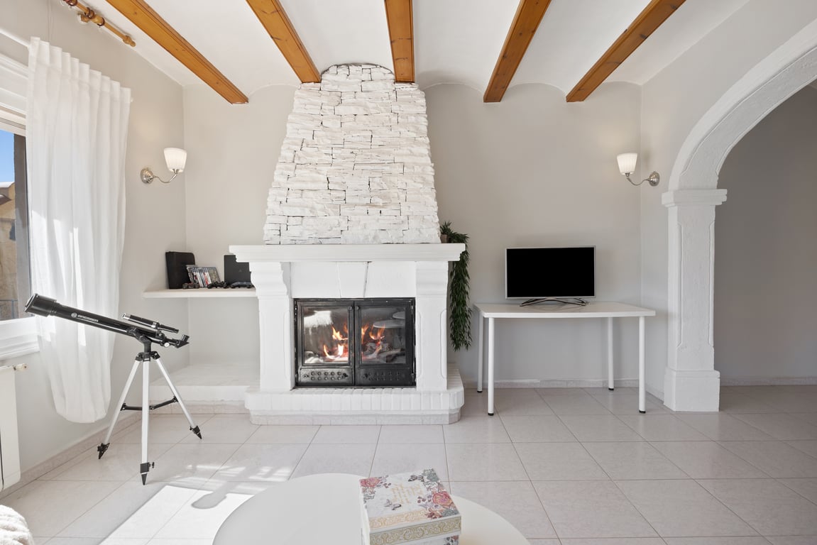Living area featuring a white stone fireplace, exposed wooden ceiling beams, and a traditional stone archway leading to adjacent rooms.