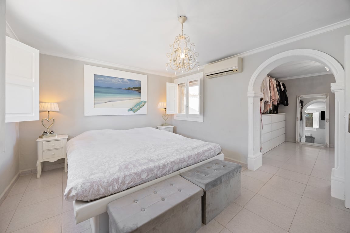 Master bedroom featuring an ensuite walk-in closet through a classic archway, tiled flooring, air conditioning, and traditional white wooden shutters.