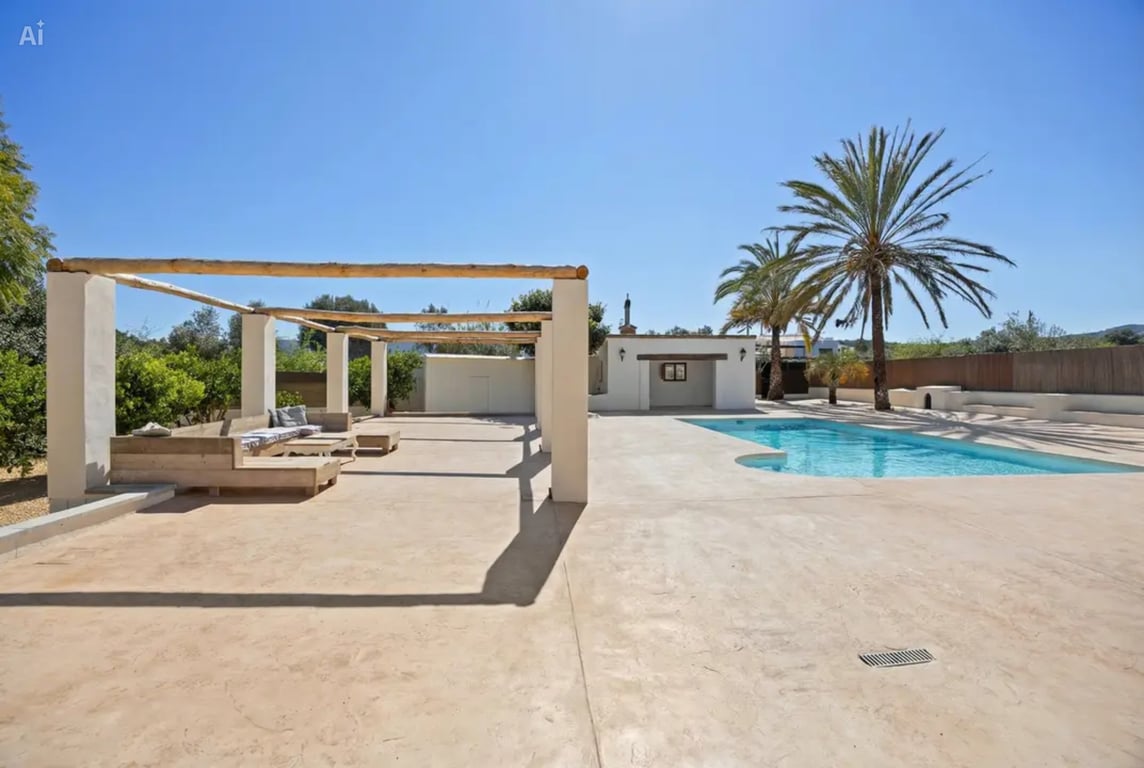 Pool area featuring a large paved terrace, a rustic wooden beam pergola with integrated seating, and Mediterranean landscaping with palm trees.