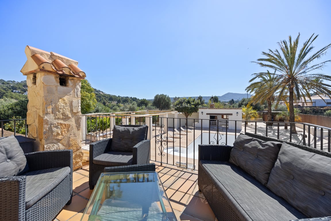 Upper terrace featuring rattan lounge furniture, terracotta tiling, and panoramic views over the swimming pool, outdoor kitchen, and Mediterranean landscape.