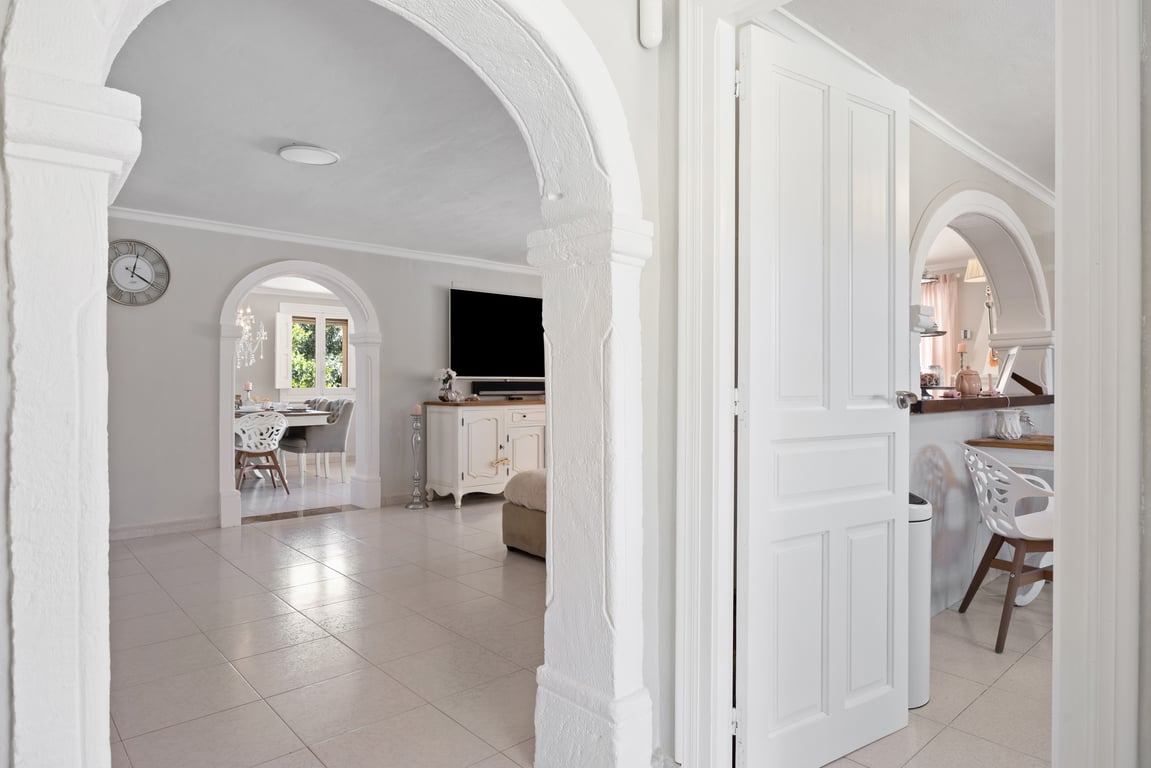 View through traditional white stone arches connecting the living area and dining room, featuring light tiled floors and bright interiors.