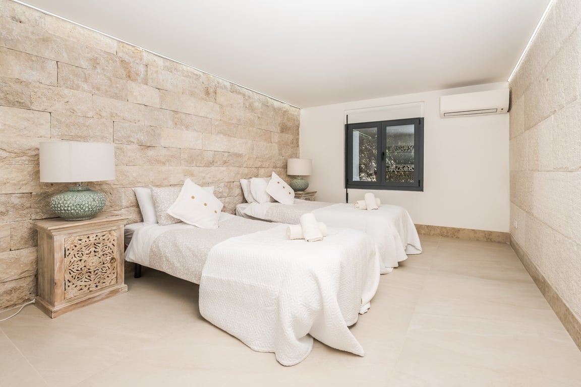 Bedroom featuring twin beds, a textured natural stone wall, carved wooden nightstands, and integrated LED ceiling lighting with air conditioning.