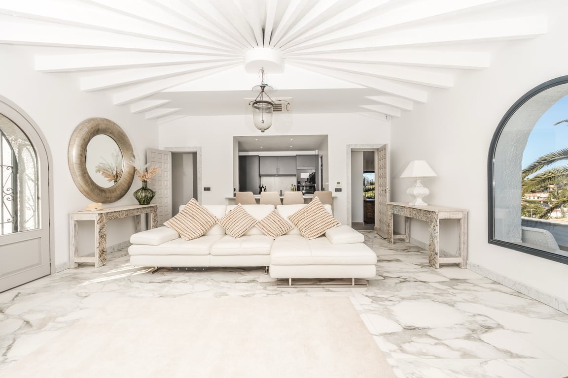Circular living area featuring radiating white ceiling beams, polished marble flooring, and large arched windows that integrate natural light and garden views.