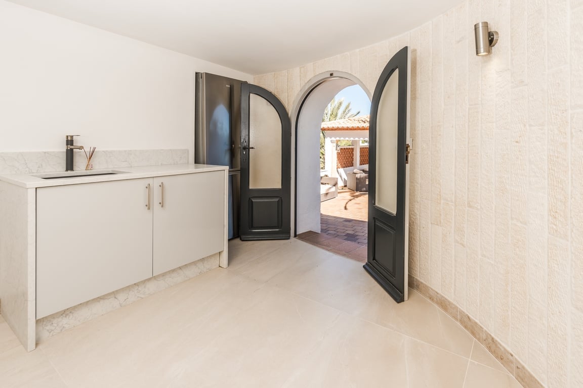 Compact kitchenette featuring marble countertops and natural stone walls, with an arched doorway leading directly to the outdoor terrace area.