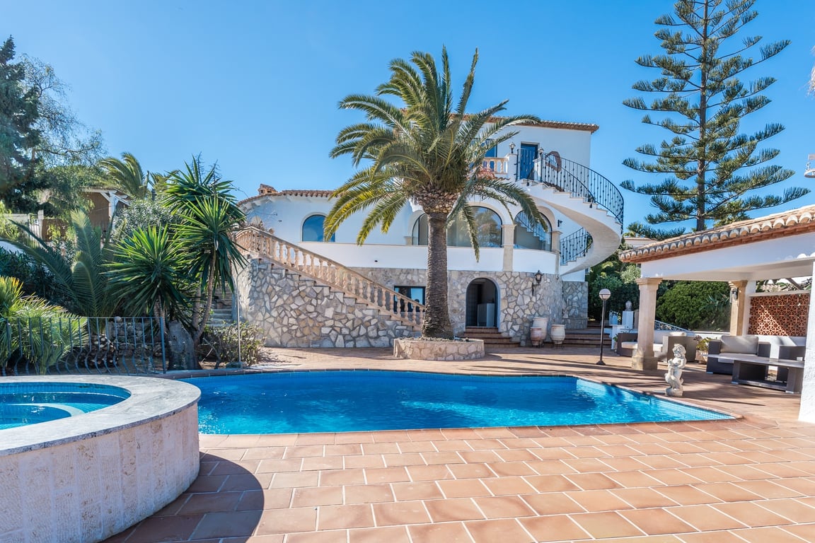 Exterior view showing the swimming pool, circular jacuzzi, and stone-clad facade. A grand spiral staircase connects the terrace levels under a clear sky.