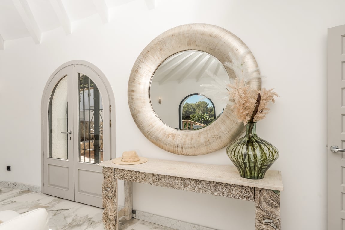 Hallway featuring marble flooring, an ornate carved console, and a large circular mirror. White beamed ceilings and arched glass doors define this bright, elegant entrance.
