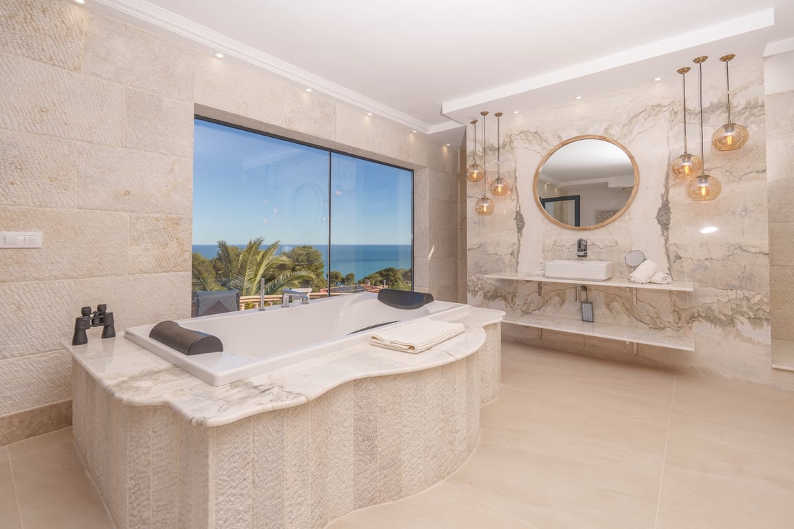 Master suite bathroom featuring a marble-clad bathtub, natural stone walls, and a large window with direct views of the Mediterranean Sea.