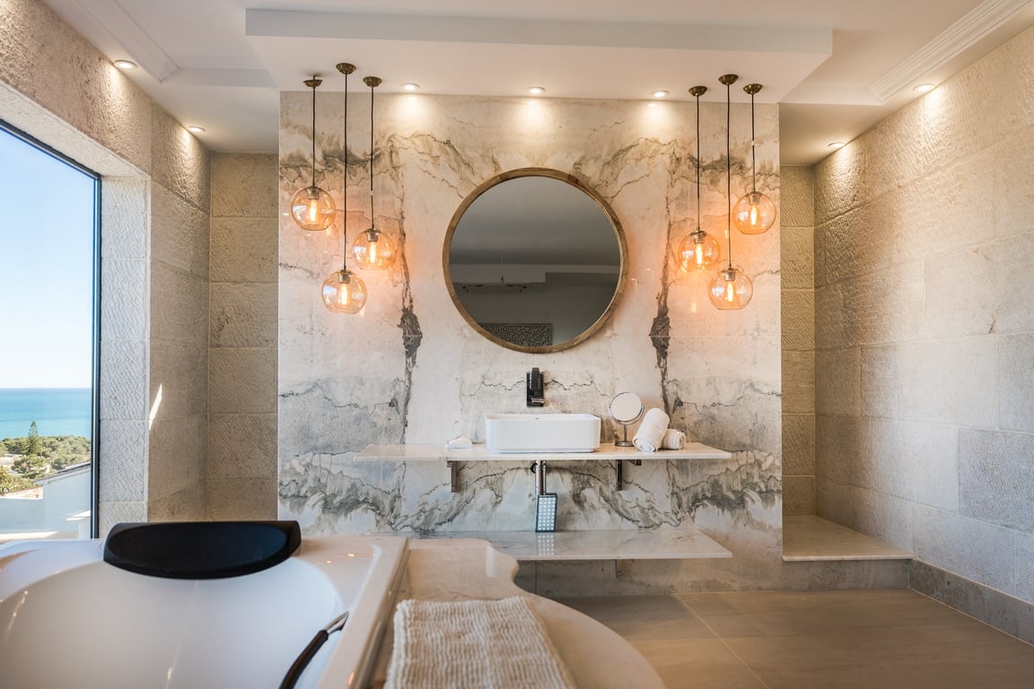 Master suite bathroom featuring natural stone walls, a veined marble vanity, spherical pendant lighting, and expansive sea views.