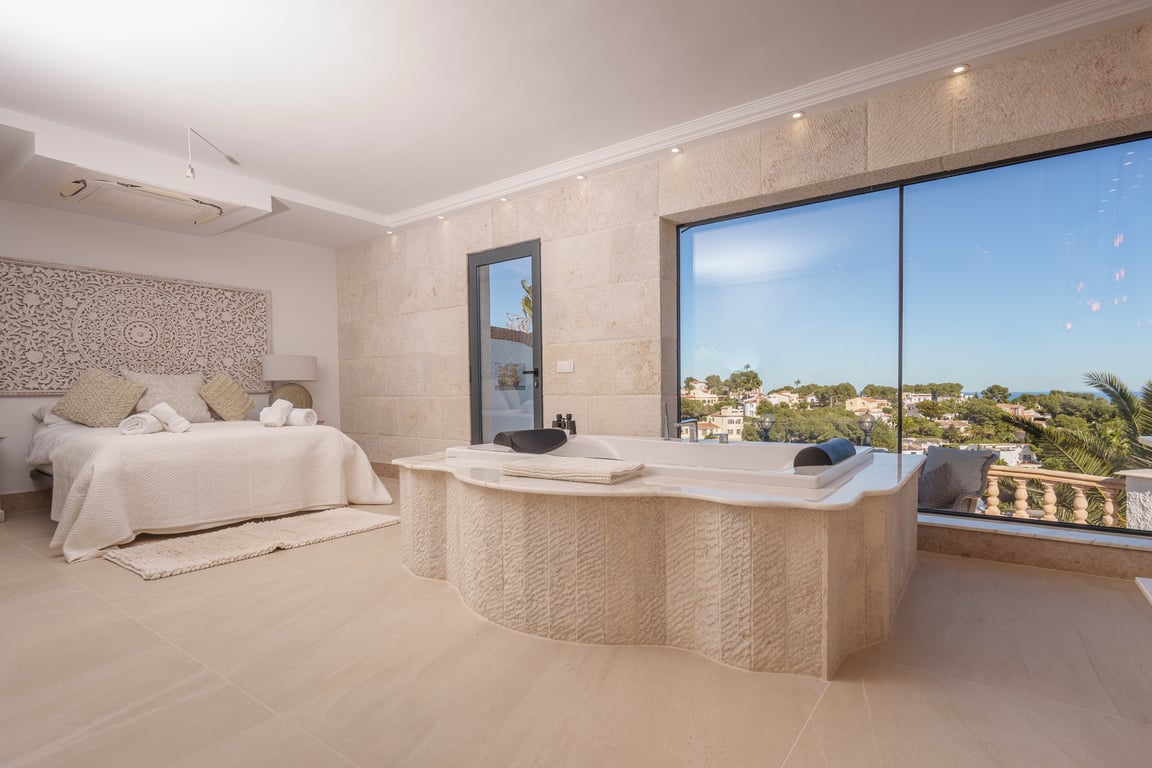 Master suite featuring an integrated bathtub with natural stone cladding, expansive windows with sea views, and a serene, open-plan layout.