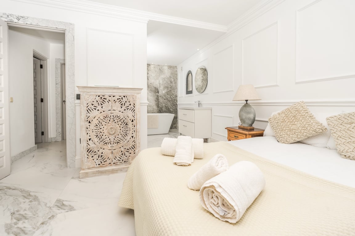 Master suite featuring an open bathroom with a freestanding tub, marble flooring, and a natural stone accent wall. Includes classic wall moldings and carved wood details.