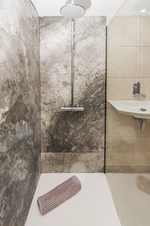 Modern walk-in shower featuring grey marble-effect wall tiles, a large chrome rain shower head, and a clean white shower tray.