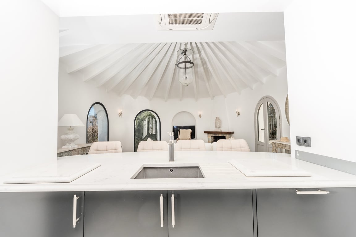 View from the kitchen island towards the circular living room, featuring a radial beamed ceiling and arched windows.