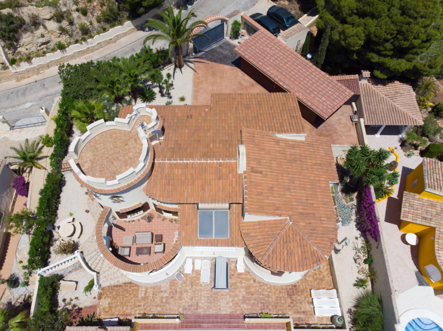 Aerial top-down view of the villa featuring its Mediterranean architecture, distinctive tower, terracotta roofs, solar panels, and expansive terraces with outdoor seating.