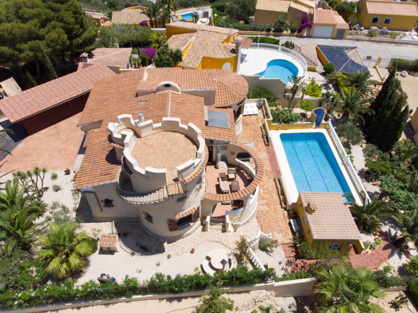 Aerial view of the villa featuring a distinctive round tower with a crenelated terrace, a large swimming pool, and multiple tiled outdoor living spaces.