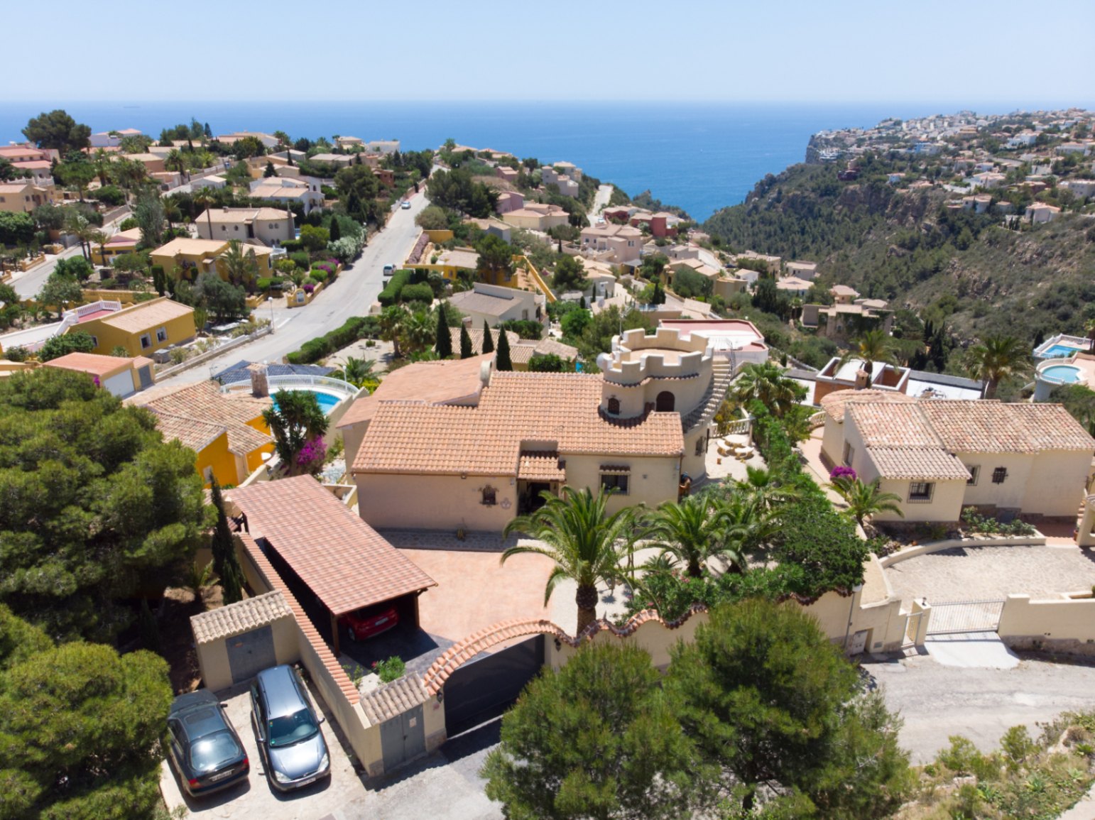 Aerial view of the villa featuring a traditional tower, spacious car port, and mature Mediterranean gardens overlooking the sea and coastal cliffs.
