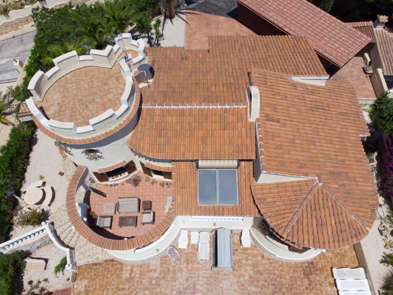 Aerial view showing the Mediterranean architecture, featuring a crenelated tower terrace, solar panels, and expansive terracotta patios with lounge seating.