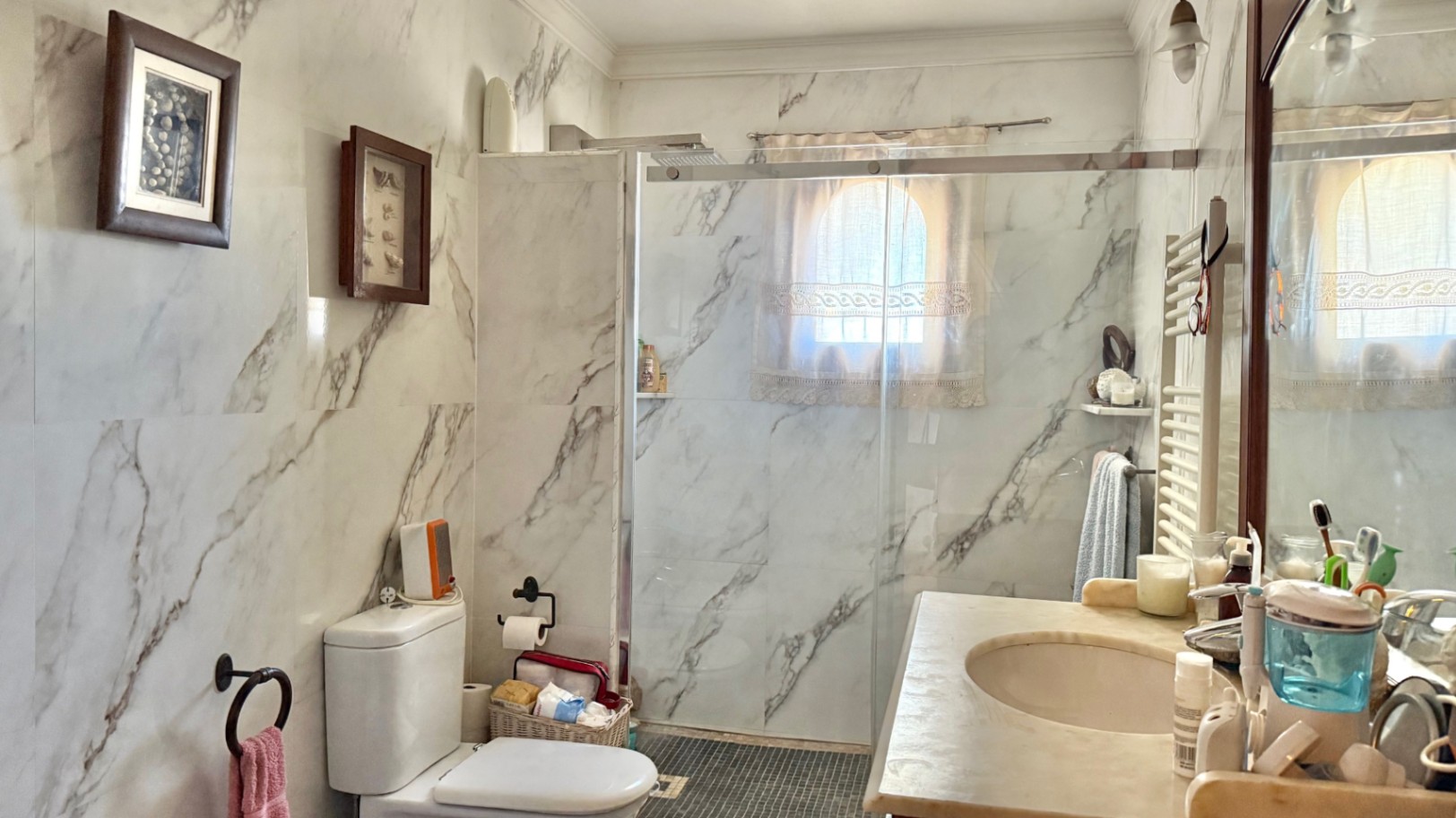 Bathroom featuring marble-effect wall tiling, a walk-in glass shower, and an arched window. Includes a built-in vanity and a wall-mounted towel radiator.