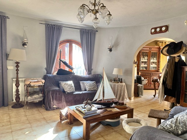 Circular living area featuring terracotta-style tiles, an arched wooden window, and a wide archway leading to the dining room, accented by nautical decor.