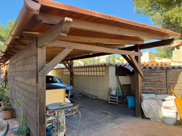 Covered wooden carport featuring exposed timber beams, a terracotta tile roof, and a durable stamped concrete driveway for vehicle parking.