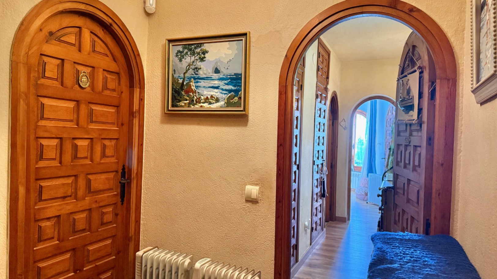 Distribution hallway featuring traditional arched doorways and solid wood paneled doors. The space includes central heating radiators and leads to the bedrooms.