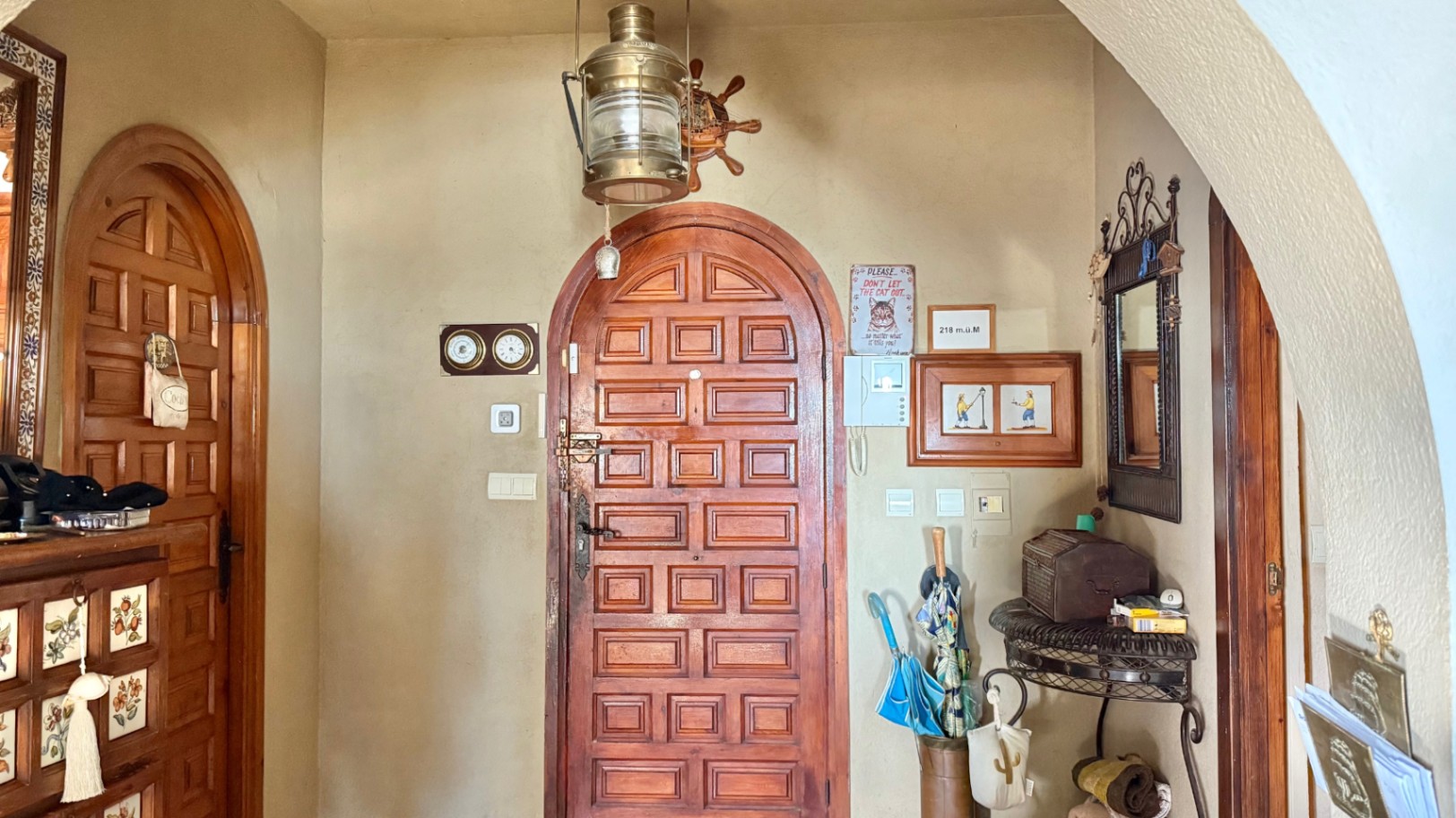 Entrance hall featuring arched solid wood doors, nautical-themed decor with a brass lantern, and wrought iron furniture set against traditional plaster walls.
