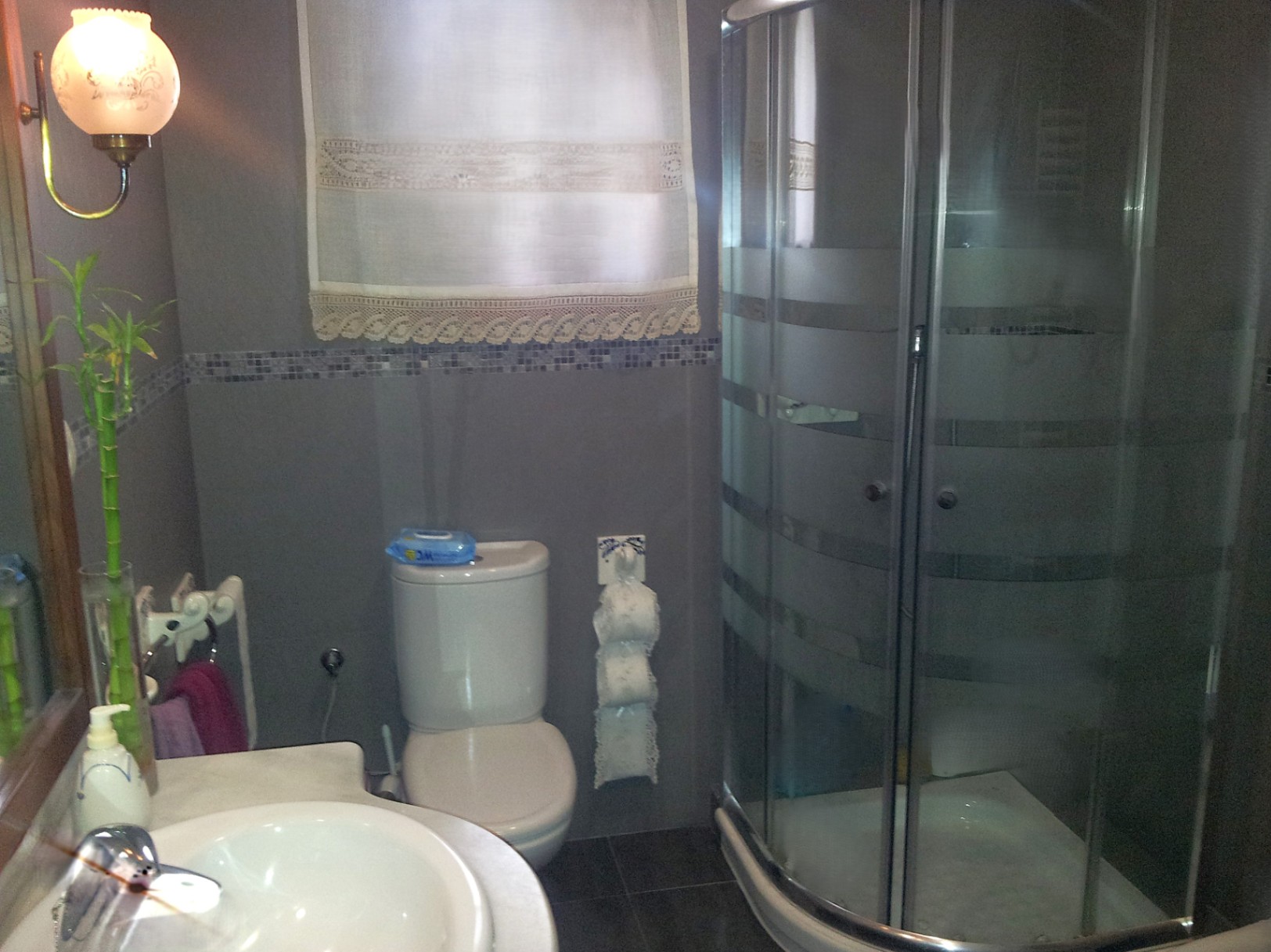 Functional bathroom featuring a curved corner shower cabin, marble sink countertop, and grey tiling with a decorative mosaic border.