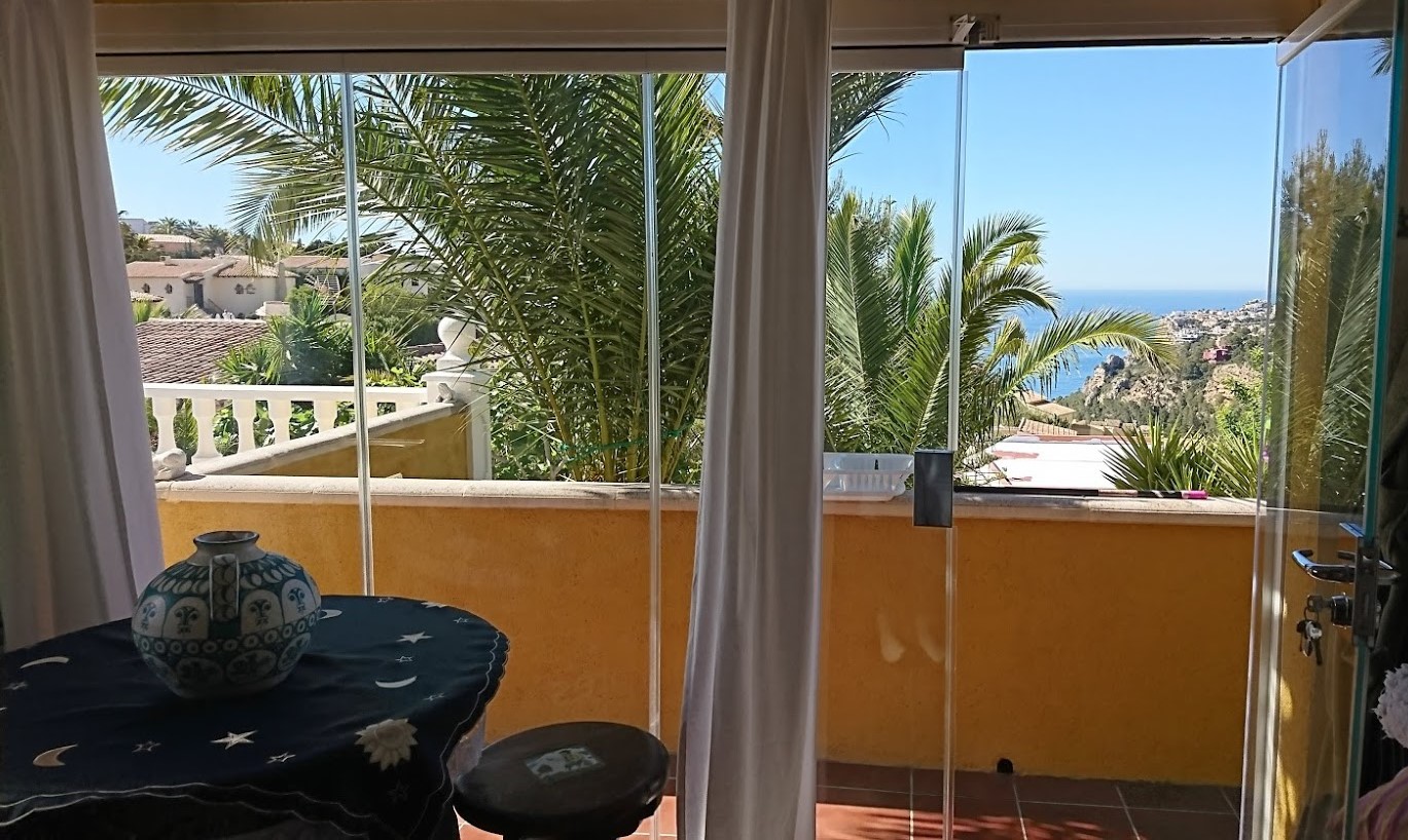 Glazed terrace featuring frameless glass curtains, providing views of the Mediterranean Sea and mature palm trees in the garden.