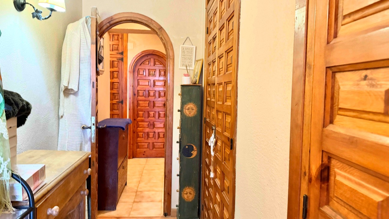Hallway featuring traditional arched wooden doorways and solid wood doors with classic paneling, complemented by neutral tile flooring.