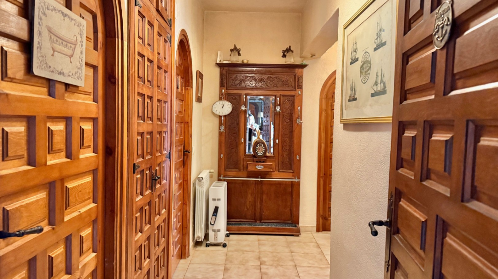 Interior hallway featuring traditional paneled wooden doors and arched entryways. A carved wooden hall stand and tiled flooring define this central distribution space.