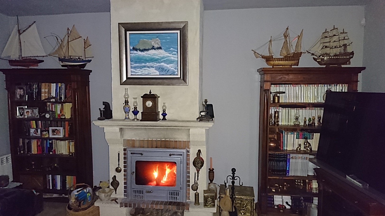 Living area featuring a wood-burning fireplace insert flanked by dark wood bookshelves displaying nautical models and a collection of books.