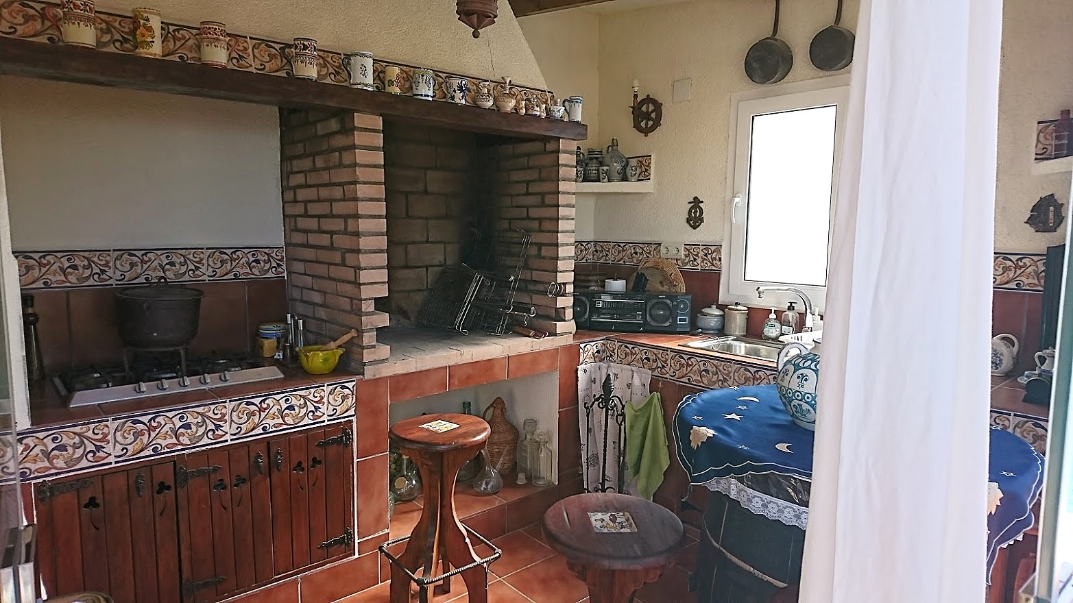 Rustic summer kitchen featuring a built-in brick barbecue, traditional tiled splashbacks, gas hobs, and dark wood cabinetry with ornate hardware.
