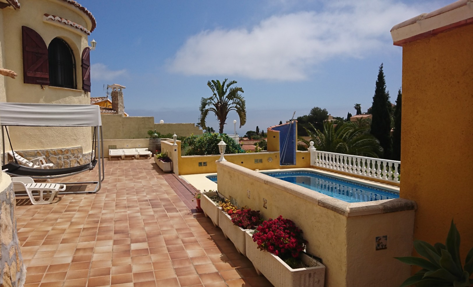 Spacious outdoor terrace with terracotta tiling, a private pool, and a Mediterranean tower feature with wooden shutters, offering ample space for sunbathing.
