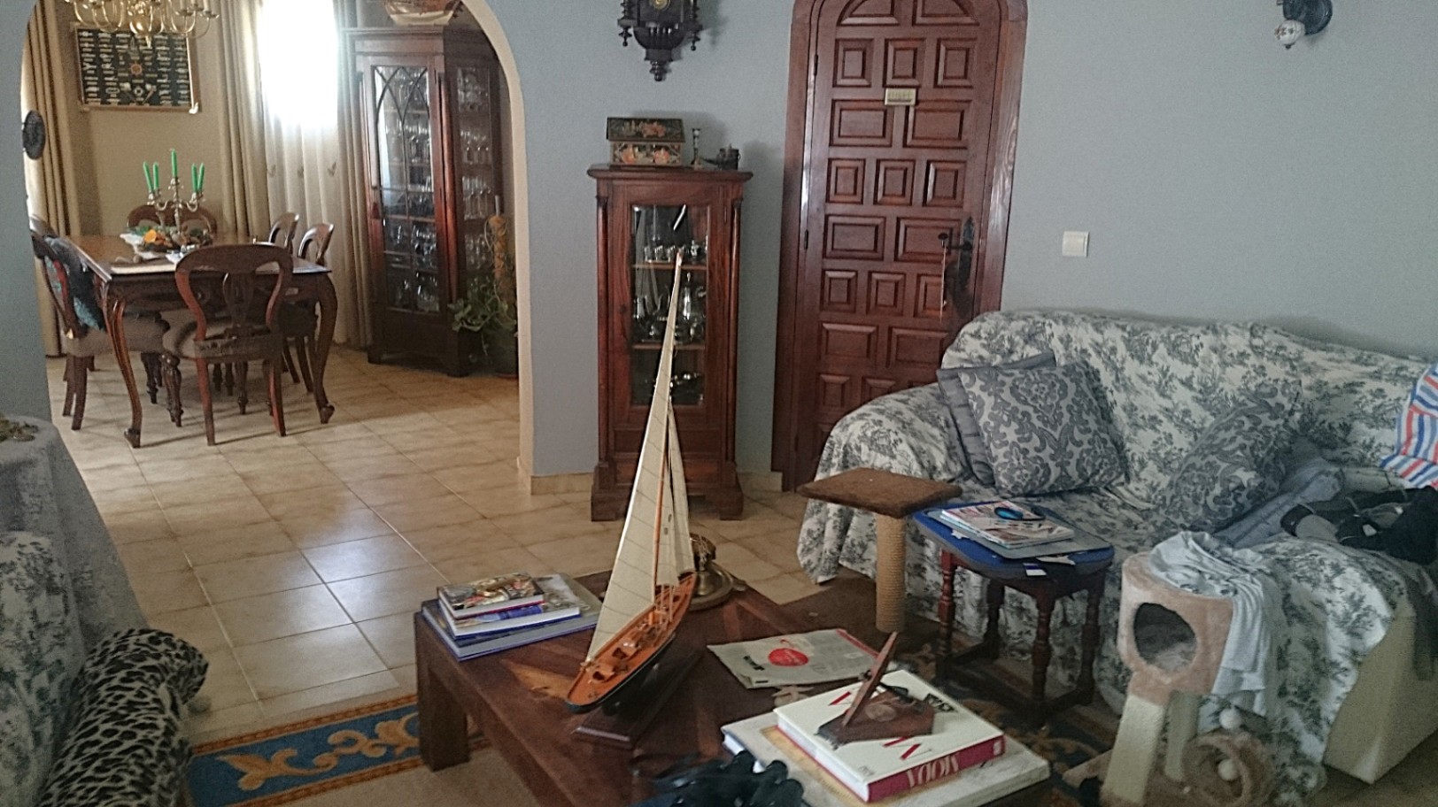 Traditional living area featuring tiled floors, classic wooden furniture, and an arched opening leading to a separate dining room with a large wooden table.