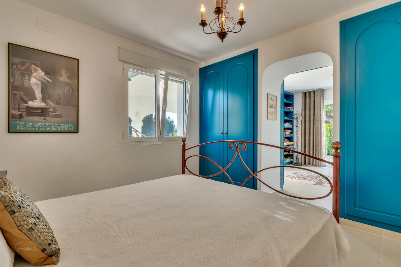 Bedroom featuring vibrant blue built-in wardrobes, a wrought iron headboard, and an arched doorway leading to a private adjoining studio.