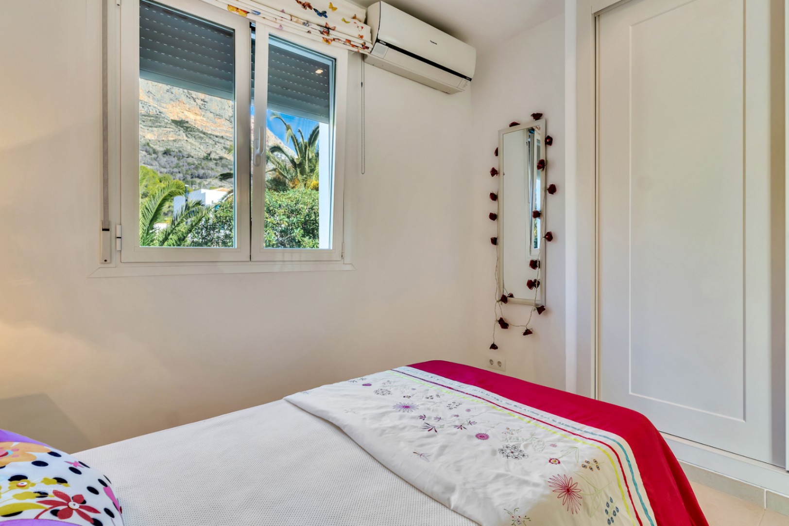 Bright bedroom featuring a built-in wardrobe, split air conditioning, and a window offering clear views of the Montgó mountain and lush palms.