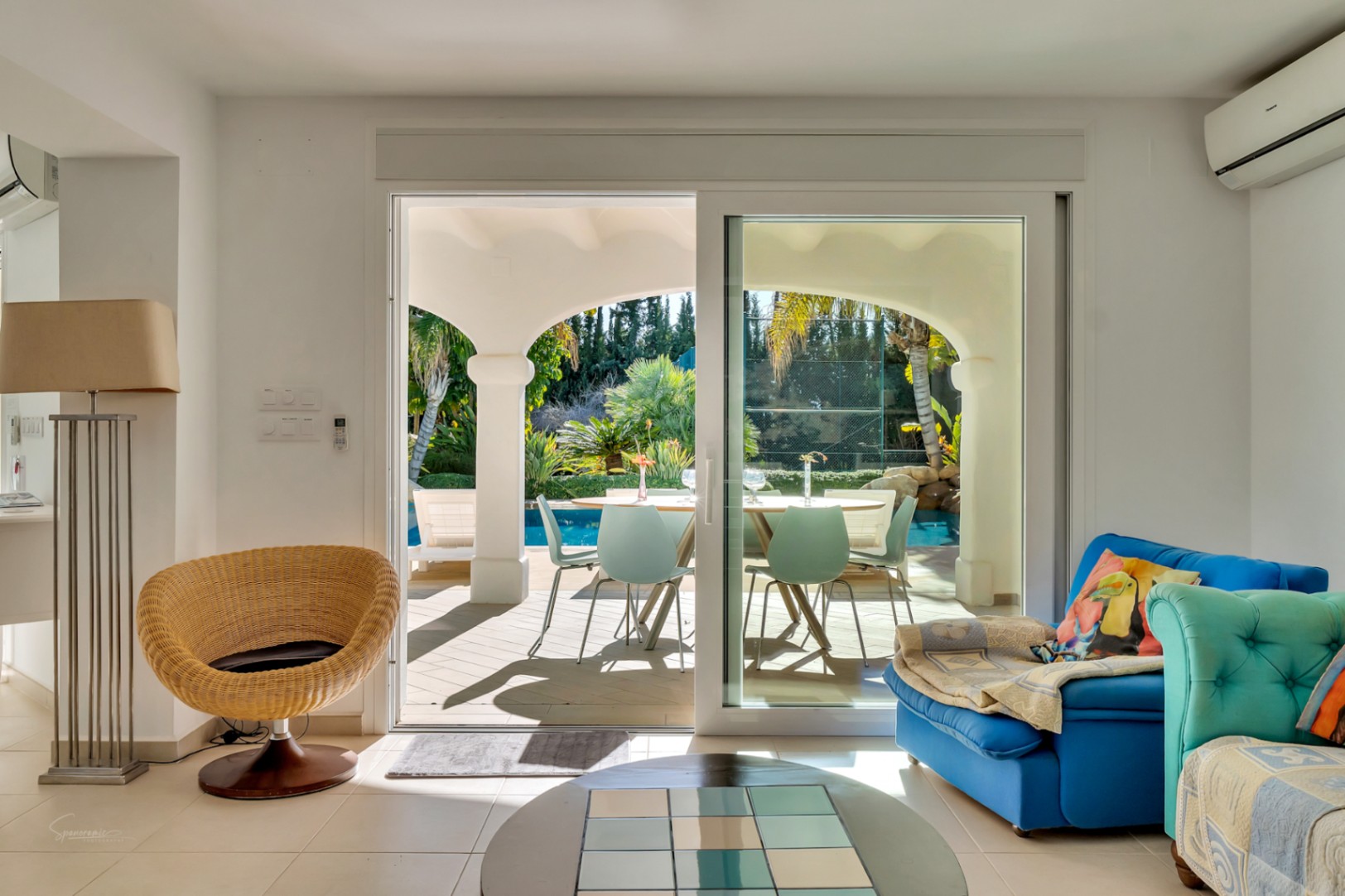 Bright living area with sliding glass doors opening onto an arched naya, featuring views of the swimming pool and private tennis court.