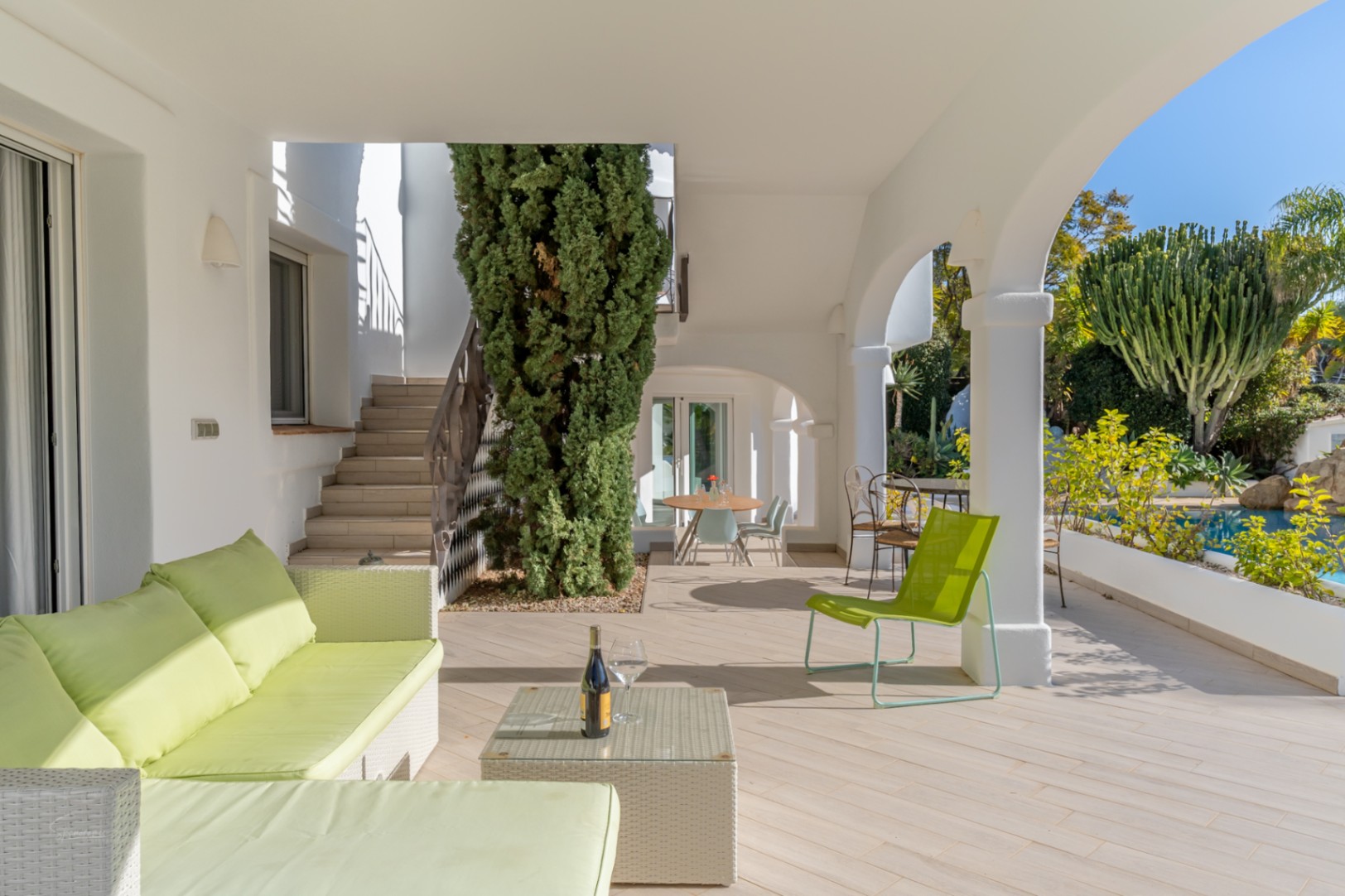 Covered naya featuring traditional white arches, lime green lounge seating, and views over the private pool and Mediterranean gardens.