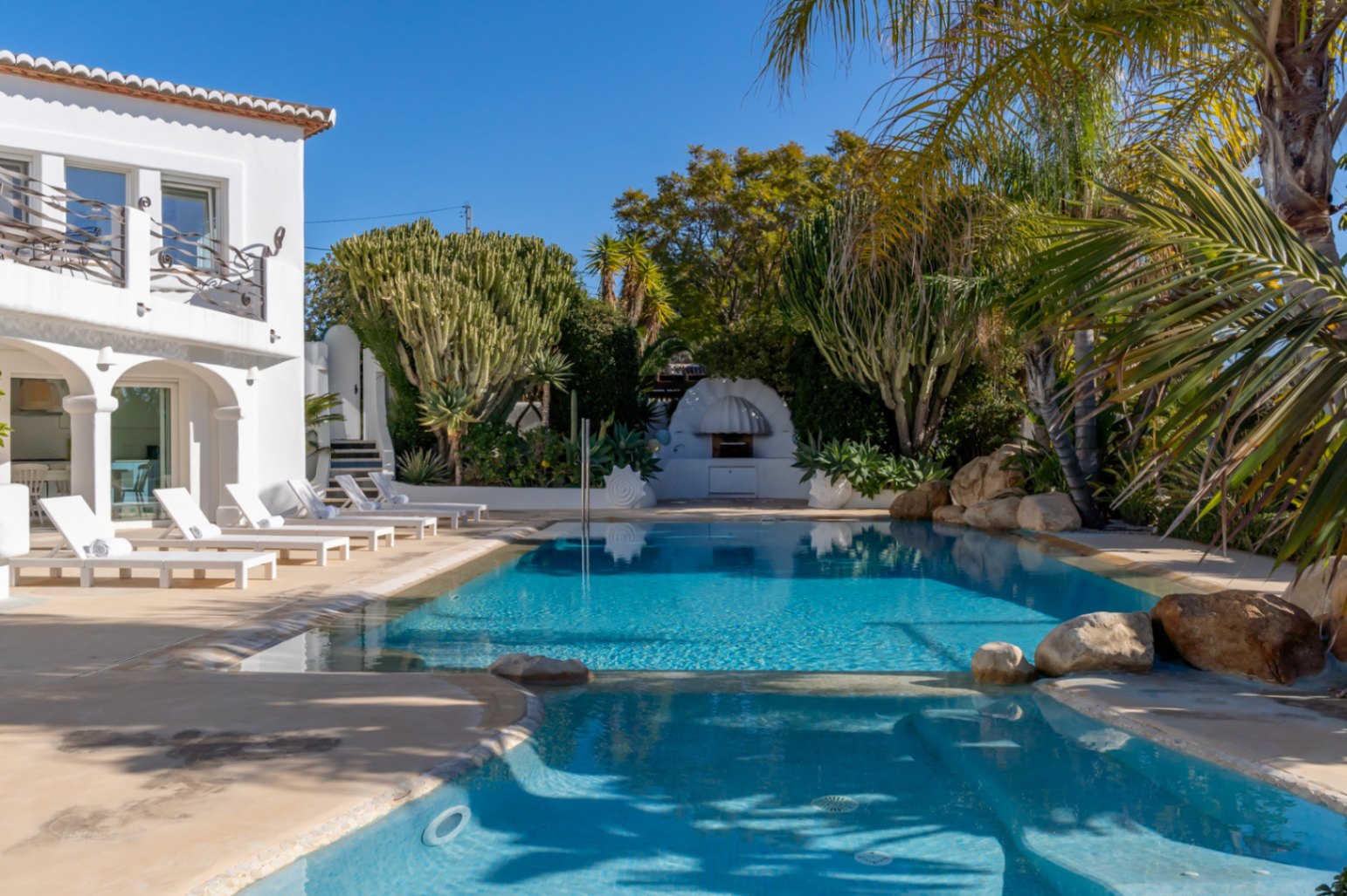 Designer swimming pool featuring a shallow hydrotherapy area, sun terrace with loungers, and a Mediterranean garden with mature cacti and a built-in BBQ.