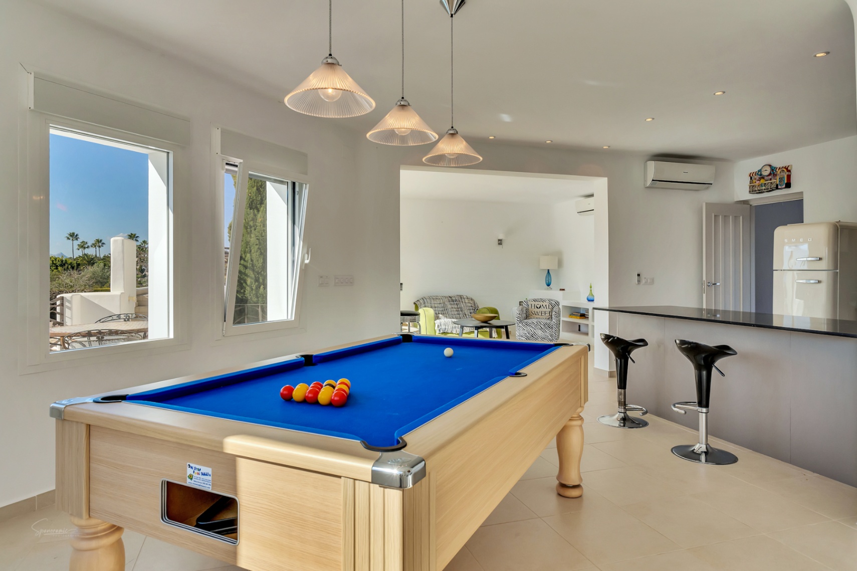 Entertainment room featuring a professional pool table, a breakfast bar with stools, and a retro-style refrigerator. Large windows provide natural light and garden views.