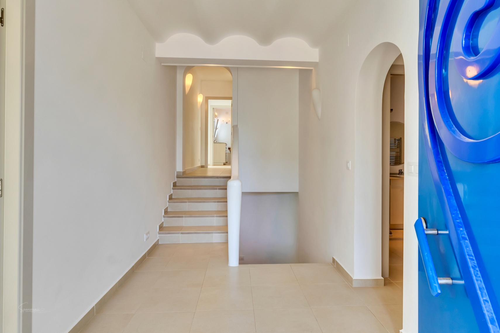 Entrance hall featuring a striking blue designer door, scalloped ceiling details, and tiled flooring connecting the villa's two levels via stairs.
