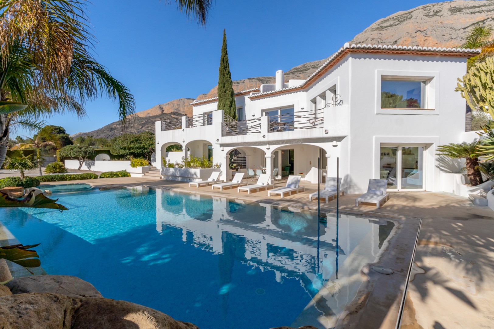 Exterior of the Ibiza-style villa featuring a 70sqm pool, arched naya, and upper terrace with designer railings against the Montgó mountain.